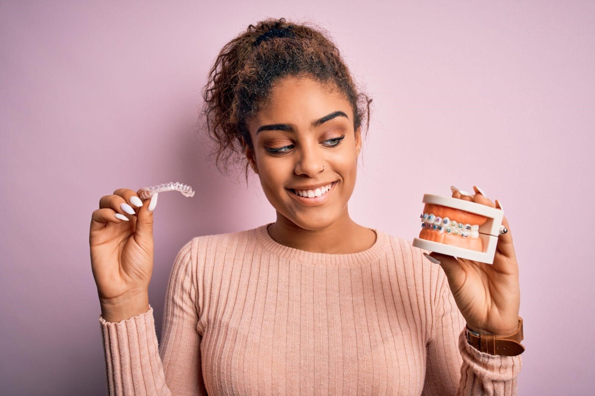 A woman in a pink shirt holding a denture model and clear aligners.