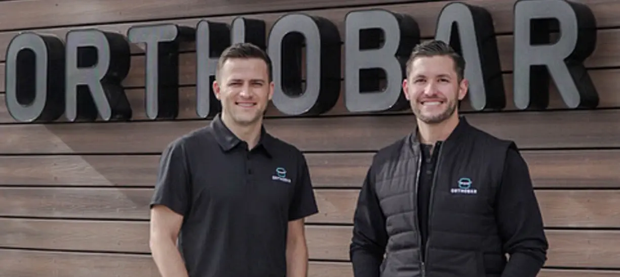 The 2 owners of Orthobar smiling in front of their orthodontic office.