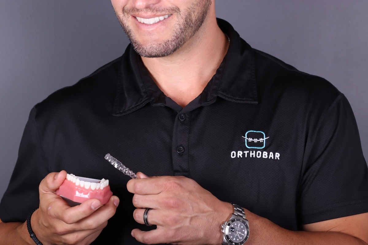 Male orthodontist holding model teeth and clear aligner.