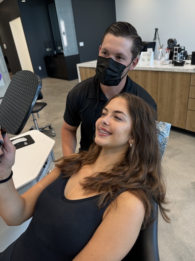 Smiling orthodontic patient wearing braces while looking into mirror.