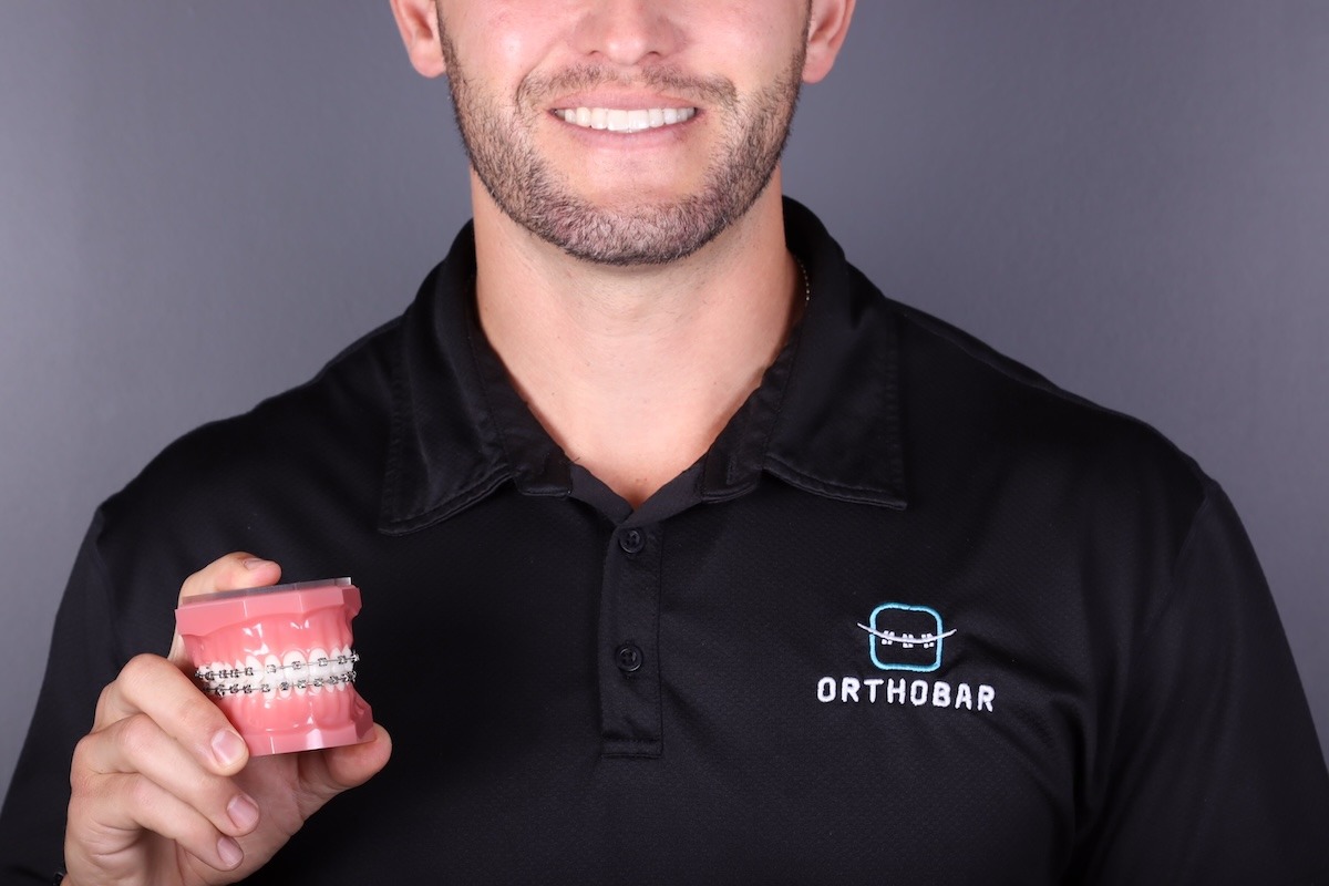 Smiling male orthodontist holding model teeth with braces.