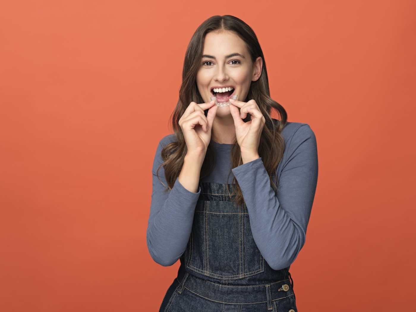 Smiling female holding clear aligners.