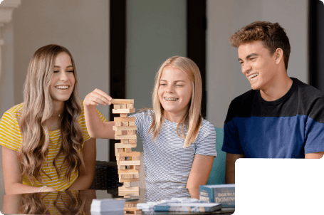 3 kids smiling while playing Jenga with straight white teeth after finishing Clear Braces treatment.