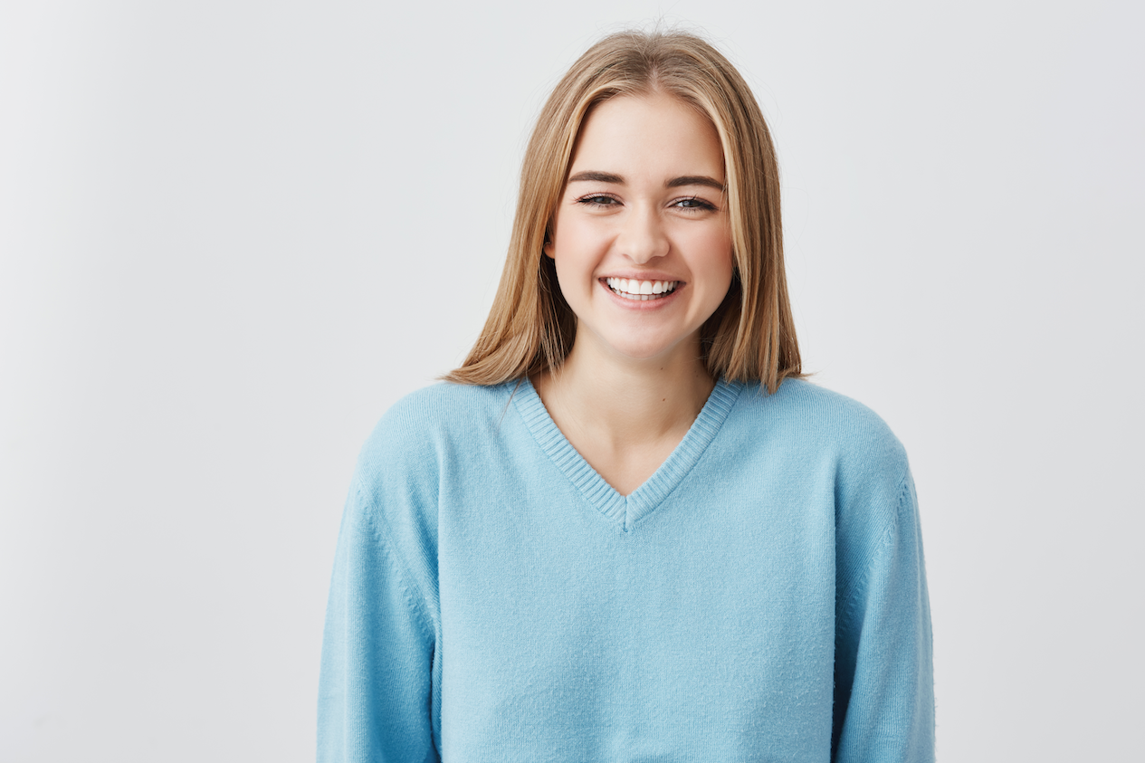 A smiling blonde girl wearing a blue sweater.