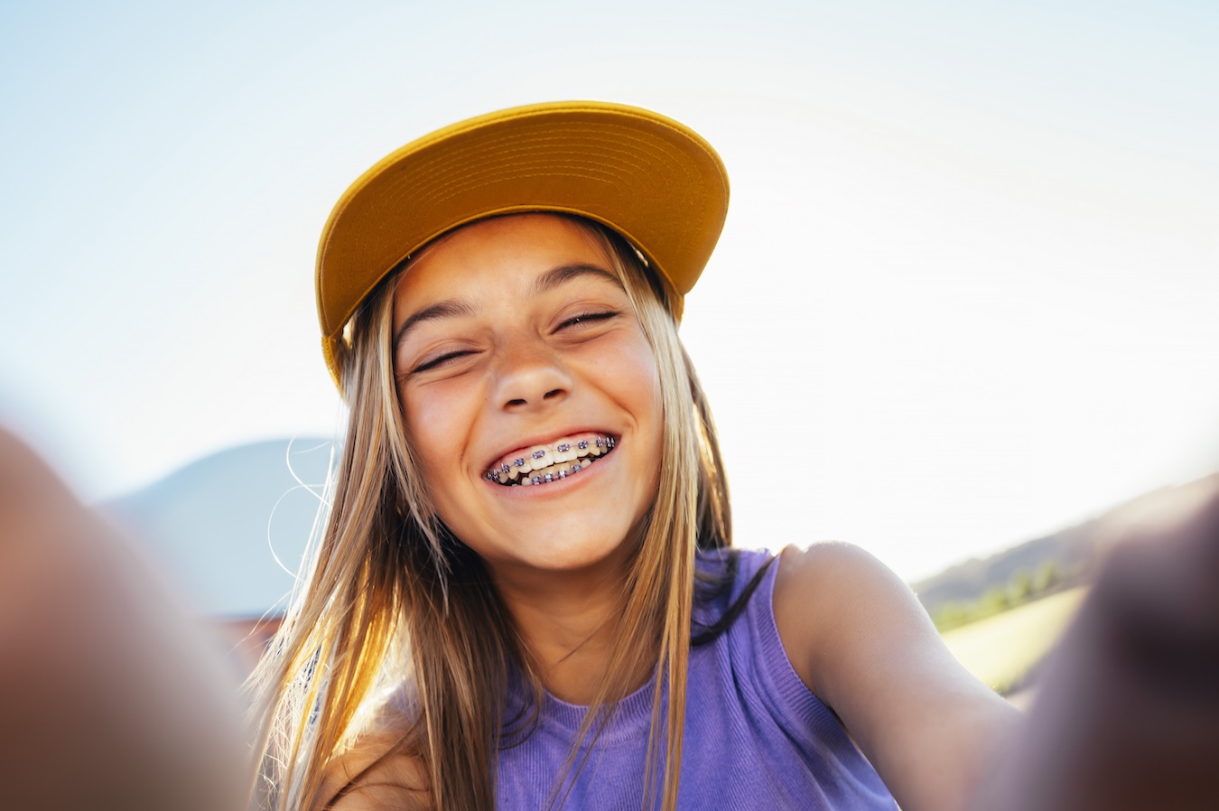 Blonde girl with braces taking a smiling selfie.