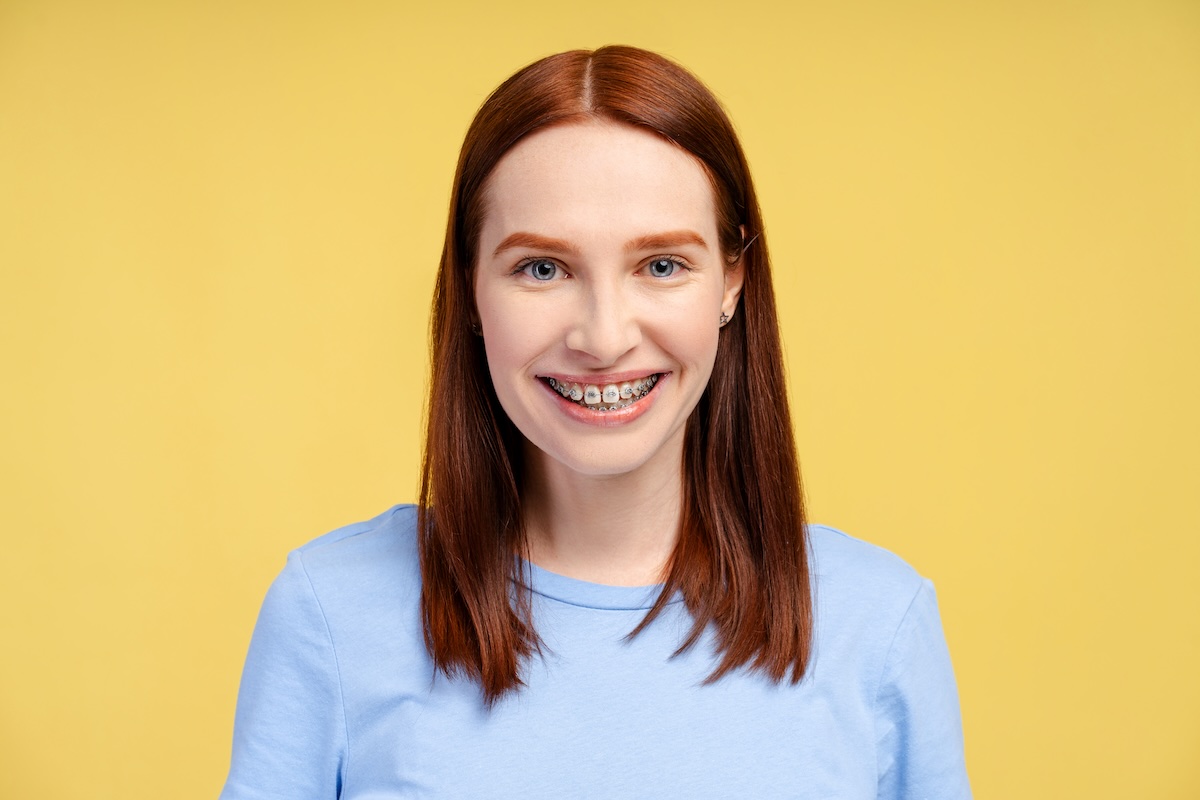 Smiling woman with braces in a blue sweater against a yellow background.