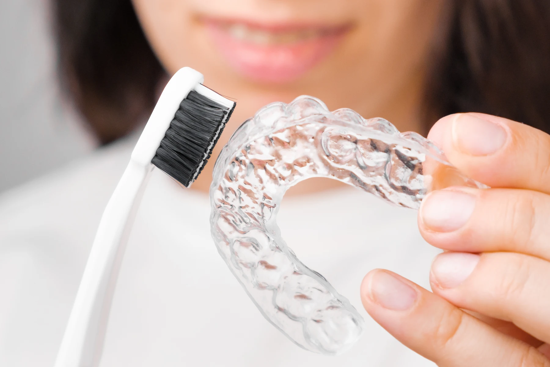 Woman cleaning a clear retainer with a soft bristled toothbrush.