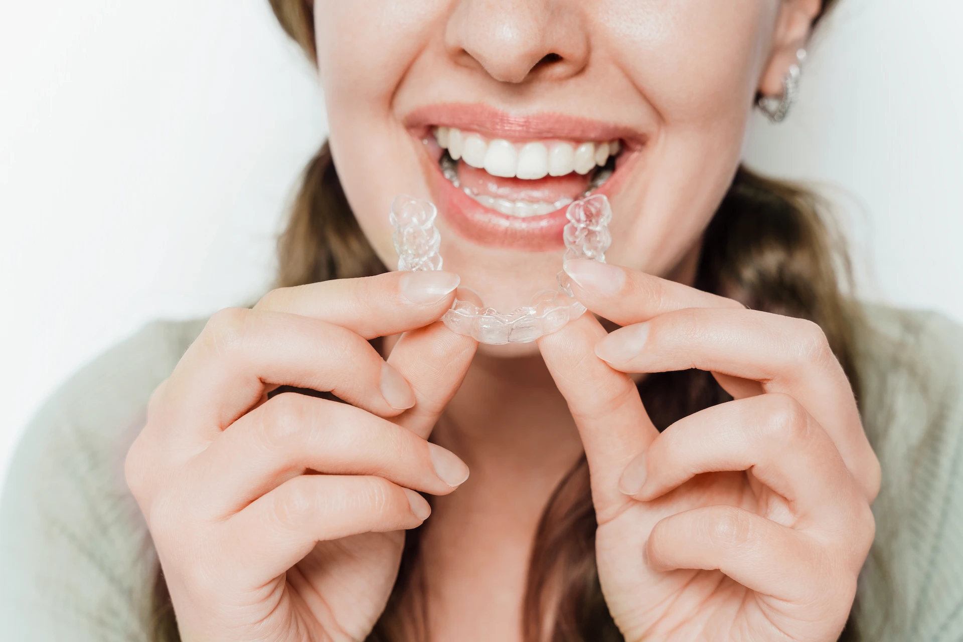 Smiling woman holding a clear aligner in front of her mouth.