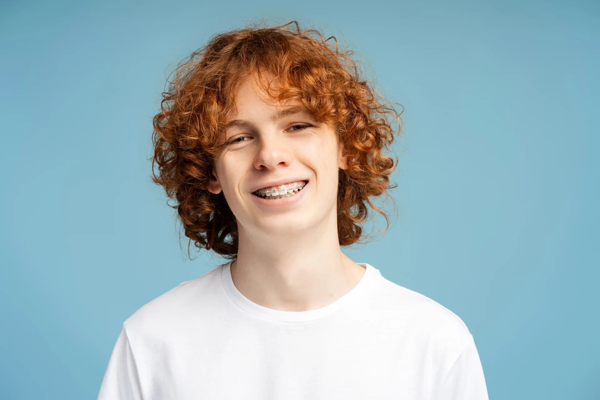 Smiling child with red hair wearing a white shirt against a blue background.
