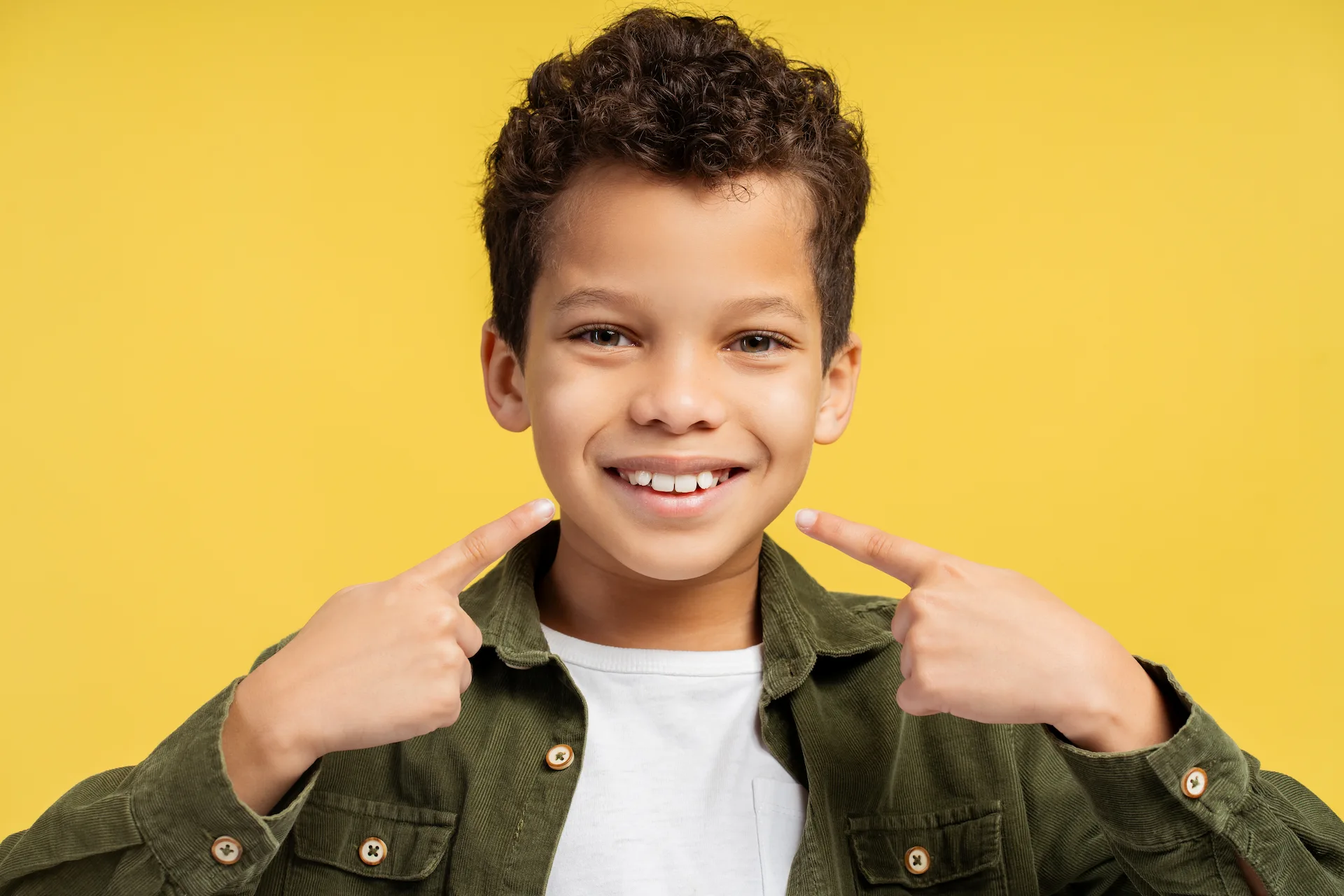 Smiling child pointing to his mouth with both hands.