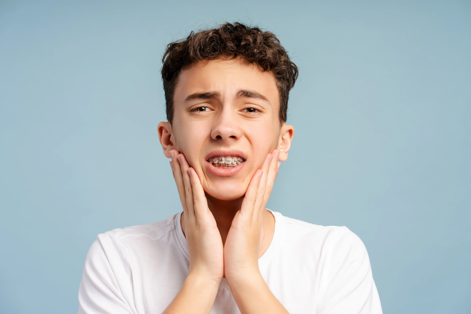 Boy with braces holding his cheek because his braces are poking them.